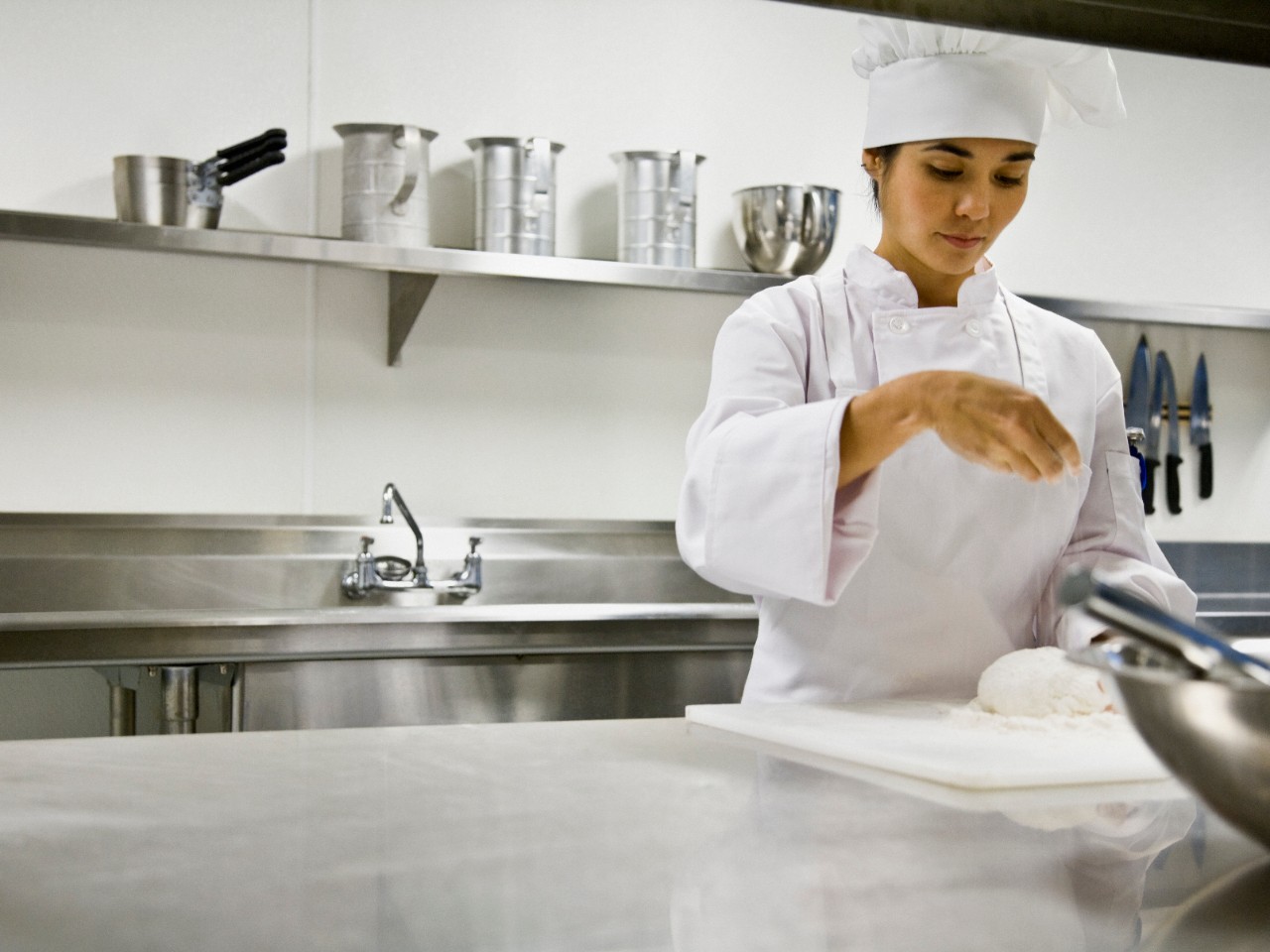 Asian female chef sprinkling flour on dough