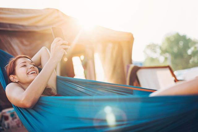 Cheerful young woman texting in the hammock in the summer, with copy space