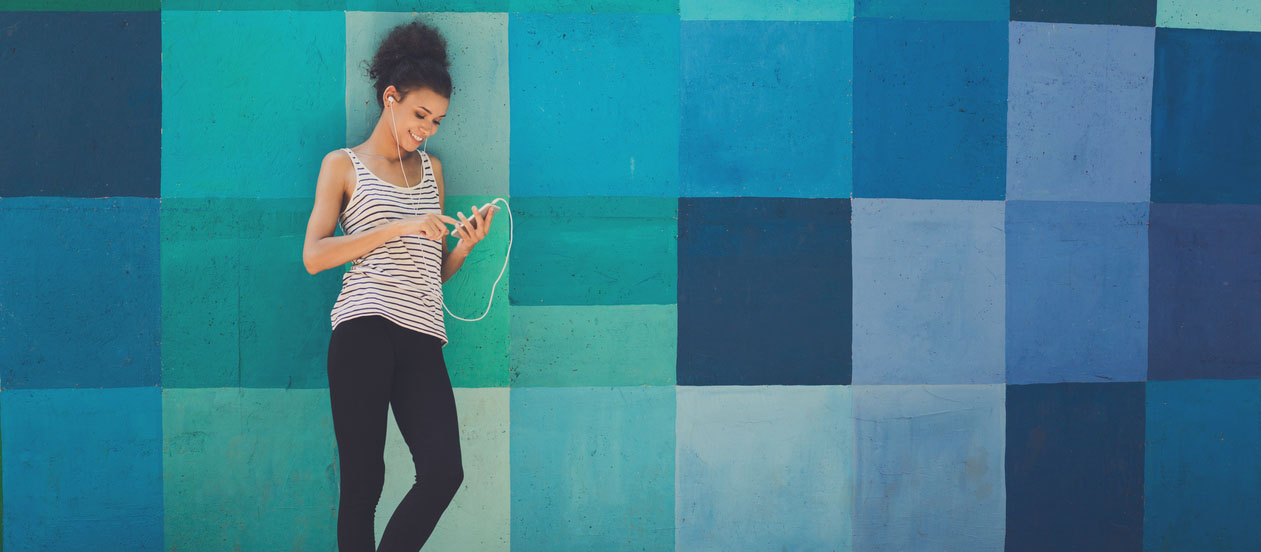 Happy smiling african-american woman leaning on bright blue graffiti wall, while listening music, relaxing from jog training, copy space