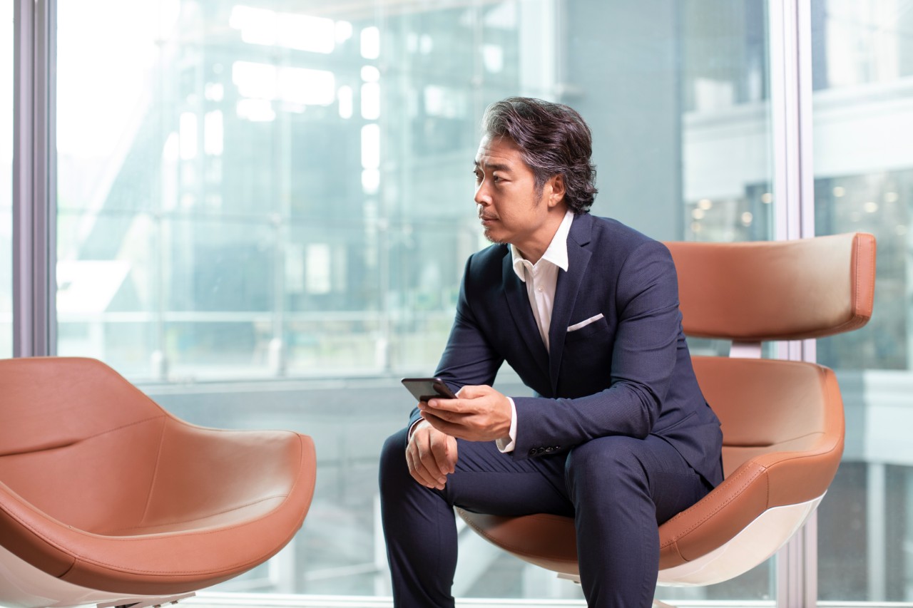 Mature Chinese businessman holding smartphone in office